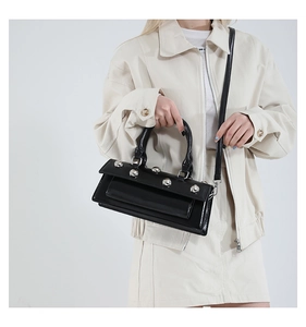 Détail du sac baguette en cuir verni noir avec clous argentés et bandoulière amovible