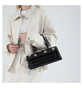 Vue détaillée du sac en cuir verni noir avec de gros rivets argentés sur le rabat