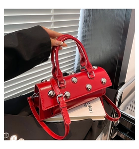Détail du sac cylindrique rouge avec rivets argentés et poignée supérieure arrondie