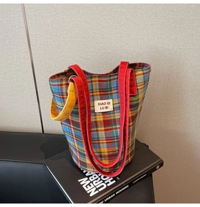 Detail of colorful plaid canvas tote bag showing red webbed handles and woven label