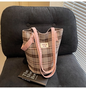 Detail of checkered canvas tote bag with pink straps on a corduroy chair and book
