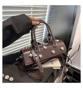 Détail d'un sac baguette en cuir marron brillant avec des rivets argentés et une bandoulière