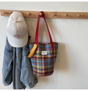 Detail of colorful plaid canvas tote bag with red strap and white brand label detail