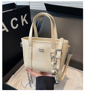 Close-up of cream leather bucket bag with silver logo and woven charm accessory