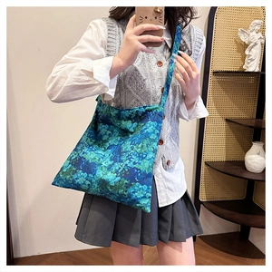 Model wearing a large floral canvas tote bag with blue and green patterns in soft indoor light