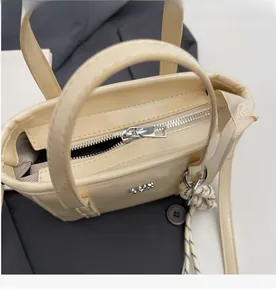 Detail view of a smooth metal zipper on a cream beige leather bucket bag with woven charm