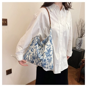Detail of canvas tote bag with blue floral patterns and brown leather strap on model