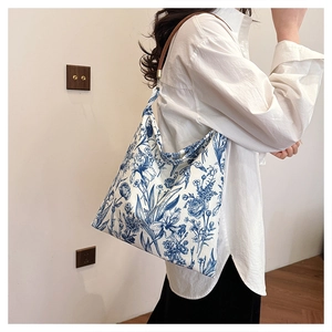 Detail of floral embroidery on a white canvas tote bag worn by a model in a minimal setting