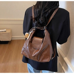 Detail showing high-quality dark brown leather texture and trendy baseball charm on the backpack