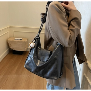 Close-up of black PU leather tote bag featuring a creative baseball charm and flap closure