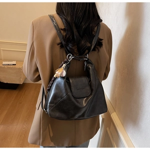 Detail of a minimalist black leather tote bag featuring a creative baseball charm accessory