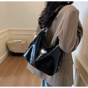 Detail der glänzenden schwarzen Hobo-Tasche mit Logo und Baseball-Schlüsselanhänger