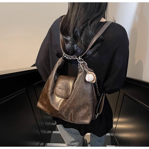 Detail view of the dark brown retro leather tote bag with a baseball charm on shoulder