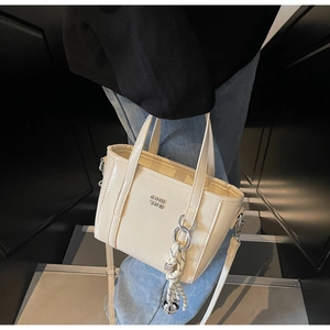 Close-up of minimalist cream bucket bag with metal letters and braided pendant detail