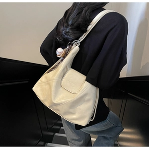 Detail view of beige soft leather tote bag with baseball charm on a model in a stairwell