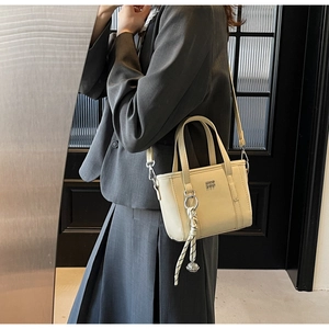 Detail of a creamy white mini bucket bag featuring woven charm and detachable shoulder strap