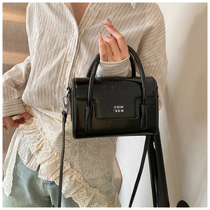 Close-up of black glossy oil wax leather handbag with stylish white decorative text detail
