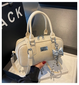 Detailed view of cream Boston bag featuring silver bow charm and textured leather finish