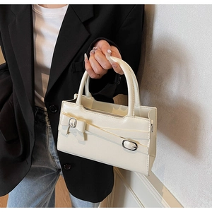 Detail of creamy white glossy leather handbag with bow decoration and metal buckle