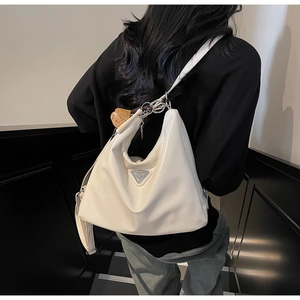 Detail der weißen PU-Leder Hobo-Tasche mit Dreiecks-Metalllogo und braunem Blattanhänger