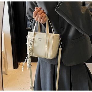 Close-up of cream mini bucket bag with silver logo and braided rope detail on grey suit