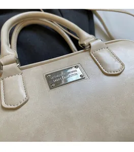 Detail of beige bowling bag showing soft leather texture and silver logo plate