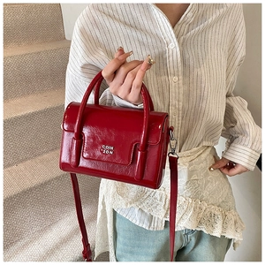 Close-up of red glossy patent leather handbag with silver logo held by a model