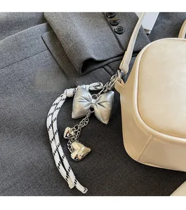 Detail of silver bow and heart charms with a woven cord on a beige leather bag