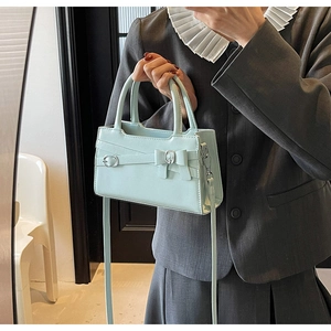 Detail of mint green handbag featuring decorative bow and silver metallic hardware clasp
