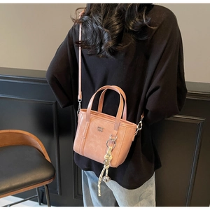 Pink PU leather bucket bag with metallic logo and decorative woven bell charm detail