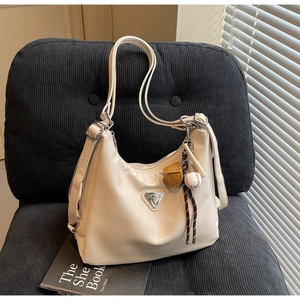 Detailansicht der cremefarbenen Ledertasche mit Metalldreieck auf schwarzem Sofa