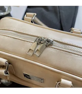 Close-up of the smooth silver dual metal zippers and brand plaque on a beige handbag
