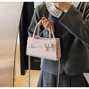 Pink minimalist handbag with bow detail worn as a crossbody bag with a grey suit
