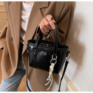 Detail of a black glossy bucket bag with silver lettering and woven charm pendant