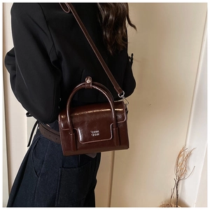 Close-up of a chocolate brown oily leather crossbody bag featuring white printed logo detail