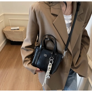 Detail of a chic black bucket bag featuring metal bells and a woven rope charm accessory