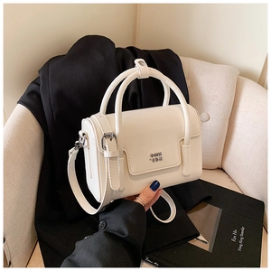 Detail view of the silver metal GOIK logo and buckle on this cream square handbag