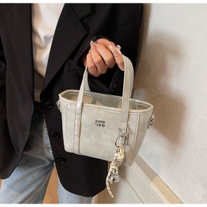 Detail of light green bucket bag with metallic logo and trendy woven charm accessory
