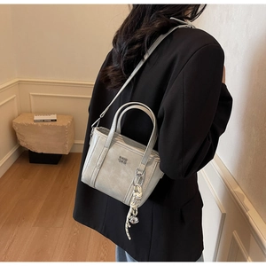 Detail of light grey leather bucket bag featuring a woven charm and detachable strap
