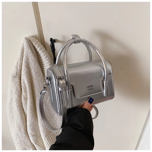 Detail of silver metallic square bag with letter embossing and adjustable strap on sweater