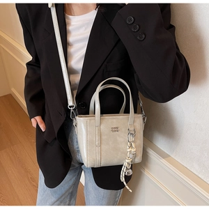 Close-up of beige bucket bag with metal logo and woven charm for office wear