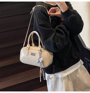 Detail of cream bowling bag featuring silver bow charm and adjustable shoulder strap