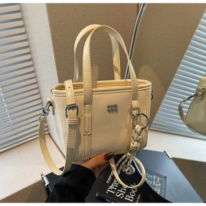 Detail of cream bucket bag showing glossy texture and elegant metal logo decoration