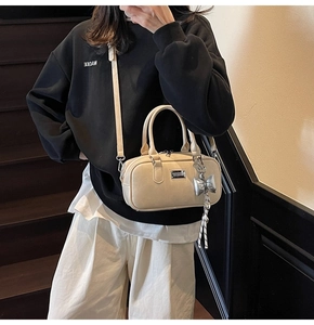 Chic beige bowling bag with silver bow charm on a model in a minimalist indoor setting