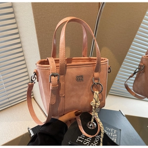 Detailed shot of pink bucket bag with metal logo, woven charm and slim leather strap