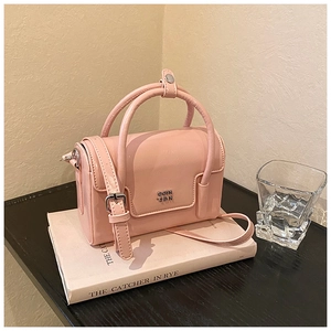 Detail of a pink leather square handbag showing the silver metal logo and adjustable strap