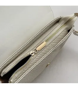 Detailed close-up of the smooth gold metal zipper on an ivory white woven shoulder bag