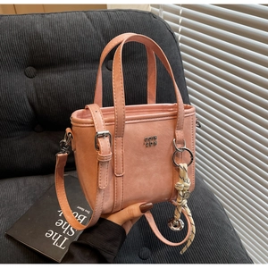 Pink minimalist bucket bag with adjustable strap and metal logo held against a sofa