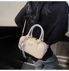 Detail of cream bowling bag with silver zipper and bow charm worn by a model