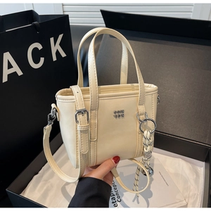 Detail of minimalist cream bucket bag with metal logo and woven pendant strap